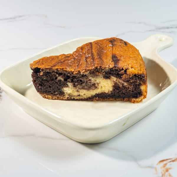 A slice of marble cake with chocolate and vanilla swirls, served on a white rectangular dish.