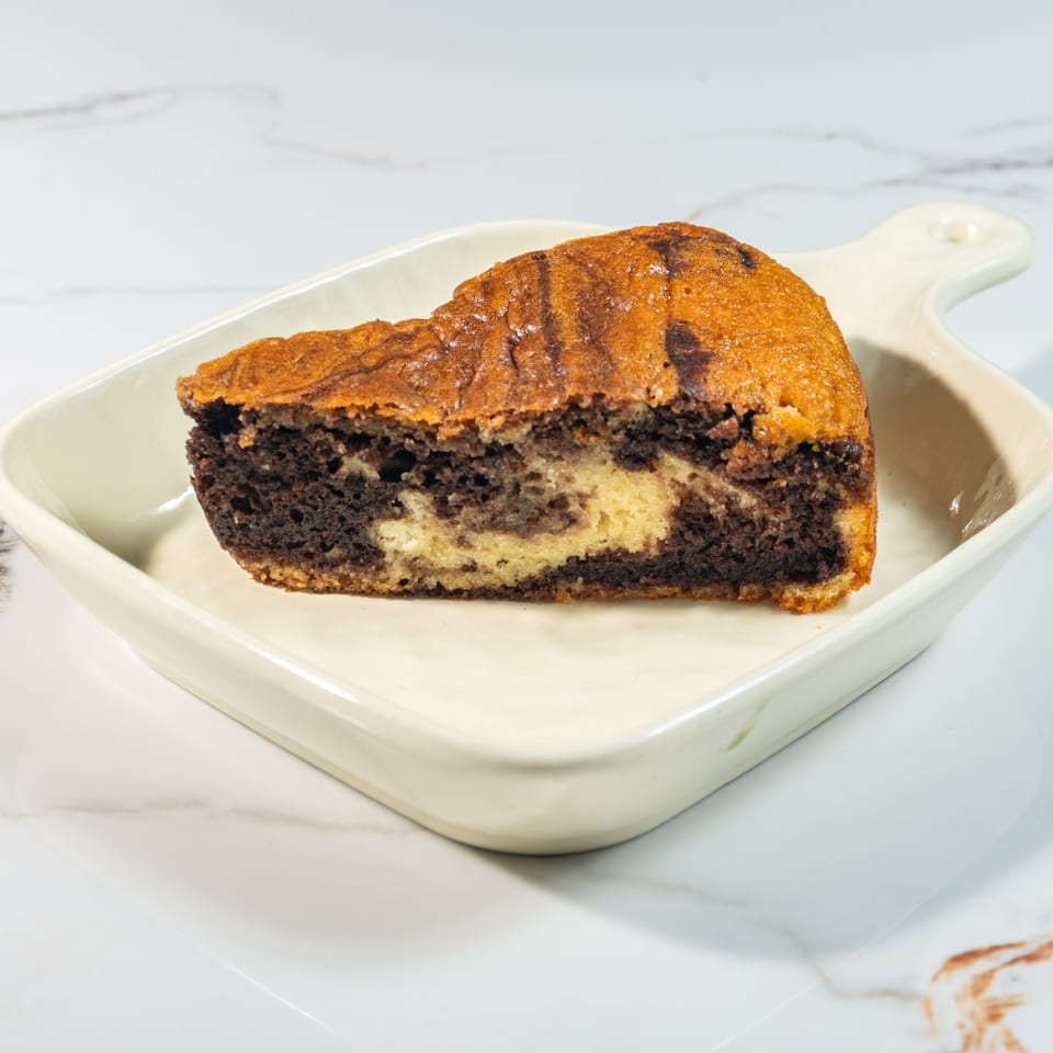 A slice of marble cake with chocolate and vanilla swirls, served on a white rectangular dish.