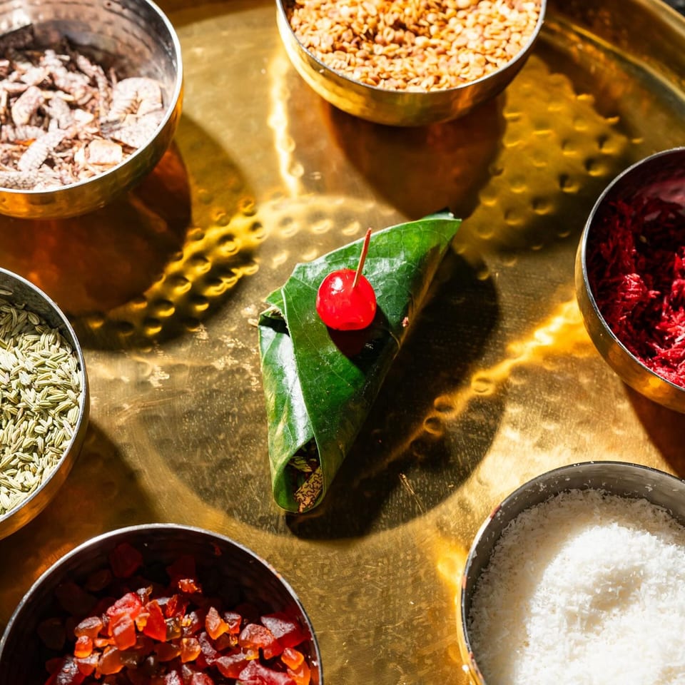 A Tikkaville paan, a betel leaf wrap with a cherry, surrounded by bowls of various ingredients.