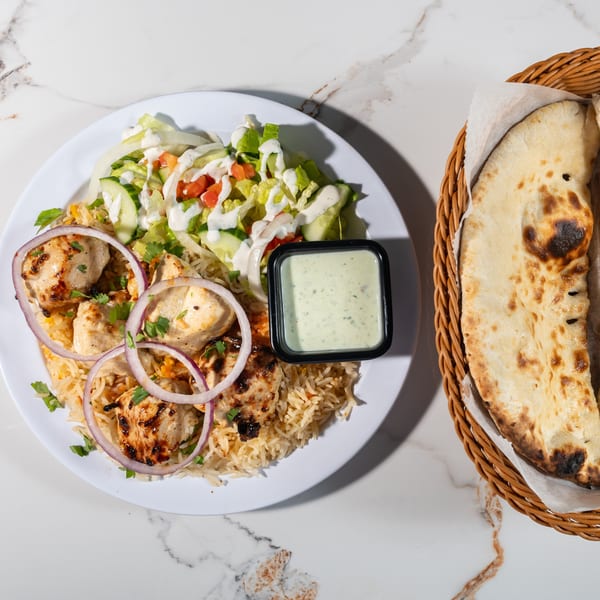 Tikkaville's chicken tikka platter with rice, salad, sauce, and a side of naan bread.
