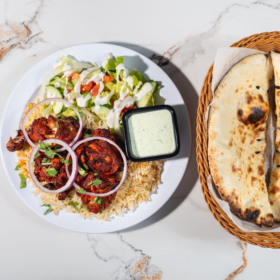 Tikkaville's chicken tikka with rice, salad, sauce, and a side of naan bread.
