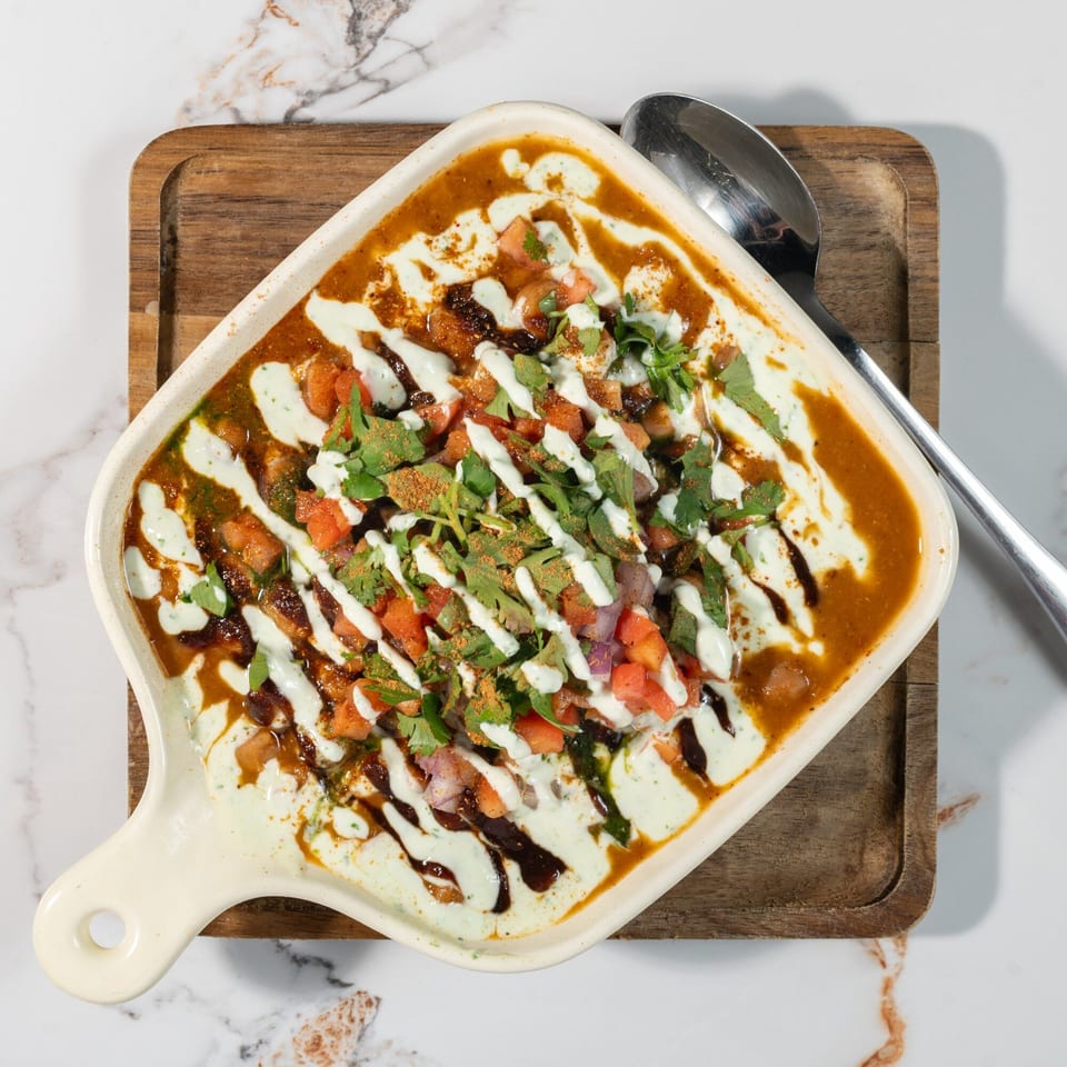 Tikkaville's Pakistani chaat, a savory dish with yogurt, chutneys, and fresh toppings in a white dish.