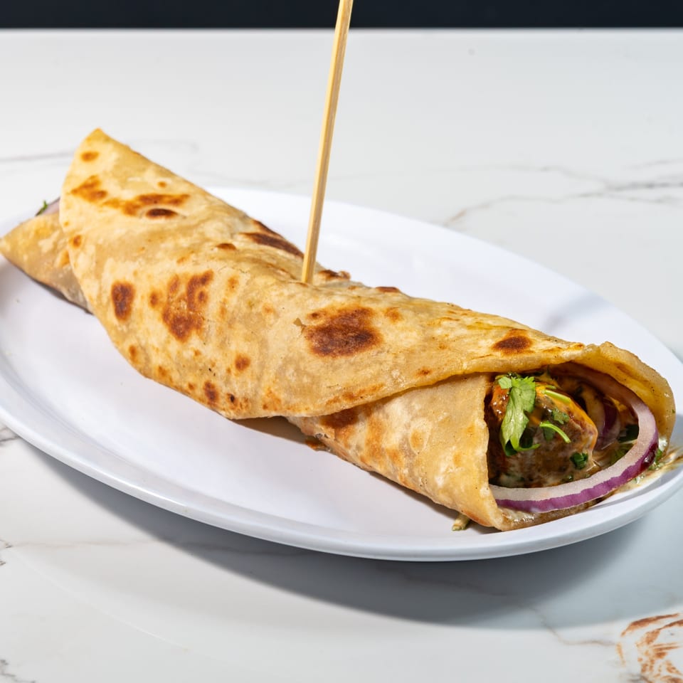 Tikkaville's Pakistani chicken tikka roll with red onions and cilantro on a white plate.