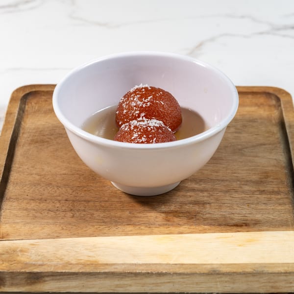 Two gulab jamun, a Pakistani dessert, in a white bowl with syrup and shredded coconut.