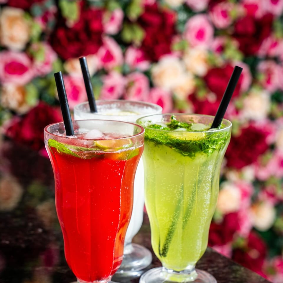 Three colorful Tikkaville drinks, red, white, and green, with straws against a floral background.